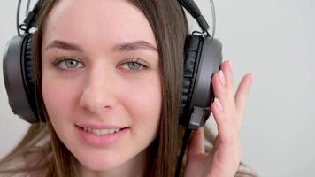 flicka i hörlurar lyssnar till musik skön grön ljus ögon närbild favorit låt på smartphone dans och sång medan njuter musik med hörlurar över vit bakgrund närbild video