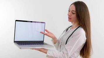 mooi jong dokter verpleegster Holding een laptop met een wit scherm in haar handen reclame een nieuw remedie behandeling voedsel supplementen presenteren in team vergadering met gebruik makend van tablet voor uitleggen video