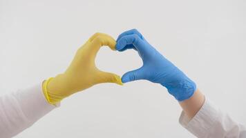 händer av en läkare i blå handskar göra en hjärta på de bakgrund av ett rörelse lampa. en sjuksköterska visar en tecken av kärlek under en pandemisk. doktorer spara människor. covid19. coronavirus video