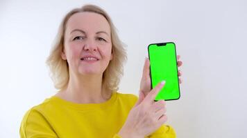magnifique femme avec téléphone vert Contexte chrominance clé souriant montrer du doigt doigt super soumissionner sourire milieu âge parfait publicité video