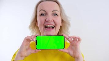 American woman stretches out hand with smartphone showing off record in mobile game or result in application with intelligence test stands in purple studio. phone green screen video