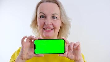 smiling woman looking at camera and pointing at green screen web template on smartphone in slow motion. Satisfied Caucasian user posing at yellow background advertising site video