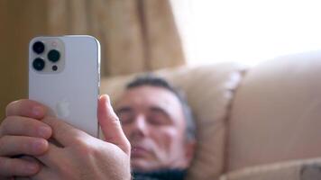 Mens gebruik makend van iphone 13 pro max. hoogte tegen wazig een Mens leugens Aan de bed resting gebruik makend van de telefoon smartphone in zijn handen comfortabel ontspannen liggen rust uit video