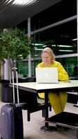 yellow suit blue suitcase at the station woman working on a laptop waiting for a plane train sitting at a table leaning on her arm watching a movie resting talking online interview solving questions video