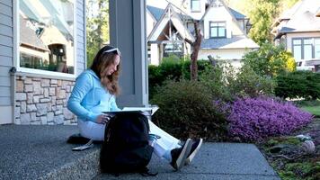sonriente dama escritura en cuaderno mientras estudiando exterior. estudiante sentado en pasos. educación en Universidad Universidad concepto. real hora video