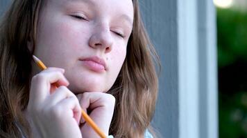 triste pensif concentré visage de une Jeune adolescent fille fille en portant une crayon dans sa mains pense en mettant il à sa bouche endroit pour texte formation école cours adolescence enfants problèmes video