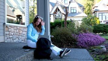 jung Frau Teenager Mädchen Sitzung auf das Veranda mit ein Aktentasche Sonnenbrille nehmen etwas aus von ihr Rucksack bekommen bereit zu tun Hausaufgaben bekommen Mittagessen Weiß Jeans Privat Quartal video