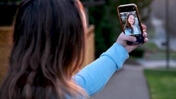 joven mujer de el latín carrera con rubia pelo tomando un foto a puesta de sol a compartir eso en social redes en un parque en primavera día. video