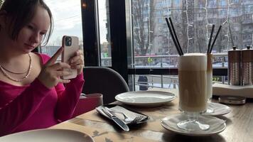 In winter, a girl takes pictures, drinks, takes off a glass of ice latte in a restaurant, stirs a cold drink video