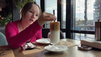 dans hiver, une fille prend des photos, boissons, prend de une verre de la glace latté dans une restaurant, remue une du froid boisson video