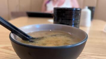 miso soep met tofu en zeewier in bruin Japans kom tegen de backdrop van een meisje een vrouw in haar handen met een menu flips de bladzijde video
