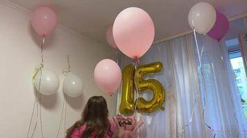 celebrate 15th birthday, teenager girl runs around the room pulling helium balloons pink white silver balloons with helium golden numbers 15 home furnishings girl in a pink jacket with her hair down video