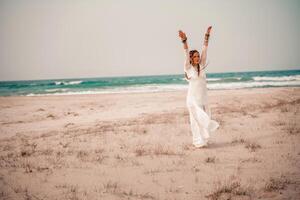 modelo en boho estilo en un blanco largo vestir y plata joyería en el playa. su pelo es trenzado, y allí son muchos esposas en su brazos. foto