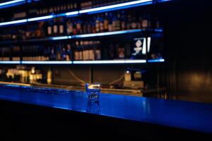 A bar with a blue counter and shelves of liquor. The bar is empty and the lights are on. photo