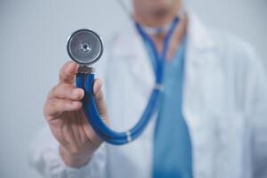 Senior doctor wearing white coat standing holding stethoscope in hands. Older male physician healthcare professional showing medical equipment ready to listen lungs or heart concept. Close up view photo