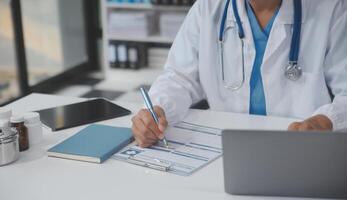 un profesional y enfocado asiático hembra médico en matorrales es trabajando y leyendo médico investigación en su ordenador portátil en su oficina a un hospital. foto