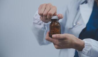 Southeast Asian medical doctor holding a bottle of pills, smiling isolated white background photo