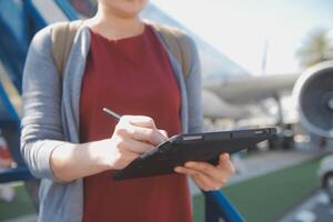 Blonde female tourist checking incoming notification on smartphone sitting on seat of airplane with netbook.Young businesswoman share media from telephone on laptop computer during plane flight photo
