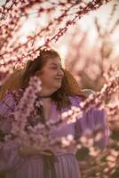 mujer floreciente melocotón huerta. en contra el fondo de un pintoresco melocotón huerta, un mujer en un largo rosado vestir y sombrero disfruta un pacífico caminar en el parque, rodeado por el belleza de naturaleza. foto