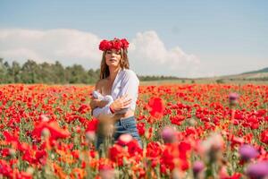 Happy woman in a poppy field in a white shirt and denim skirt with a wreath of poppies on her head posing and enjoying the poppy field. photo