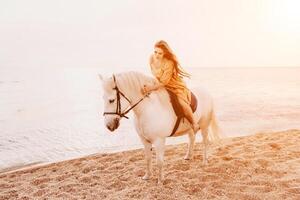 A woman in a dress stands next to a white horse on a beach, with the blue sky and sea in the background. photo