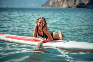 Woman sap sea. Sports girl on a surfboard in the sea on a sunny summer day. In a black bathing suit, he lies on a sap in the sea. Rest on the sea. photo