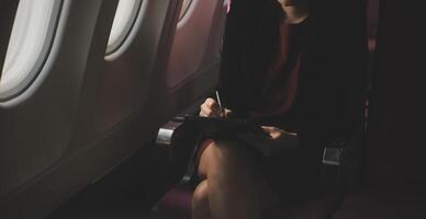 Blonde female tourist checking incoming notification on smartphone sitting on seat of airplane with netbook.Young businesswoman share media from telephone on laptop computer during plane flight photo