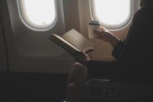Blonde female tourist checking incoming notification on smartphone sitting on seat of airplane with netbook.Young businesswoman share media from telephone on laptop computer during plane flight photo