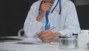 un profesional y enfocado asiático hembra médico en matorrales es trabajando y leyendo médico investigación en su ordenador portátil en su oficina a un hospital. foto