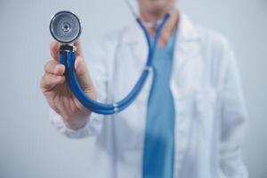 Senior doctor wearing white coat standing holding stethoscope in hands. Older male physician healthcare professional showing medical equipment ready to listen lungs or heart concept. Close up view photo