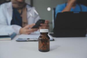 asiático psicólogo mujer señalando en pastillas botella a explicando medicina y prescripción a hembra paciente mientras dando asesoramiento acerca de médico y mental salud terapia a hembra paciente en clínica. foto