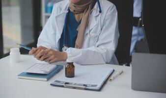 asiático psicólogo mujer señalando en pastillas botella a explicando medicina y prescripción a hembra paciente mientras dando asesoramiento acerca de médico y mental salud terapia a hembra paciente en clínica. foto