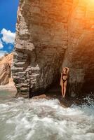 Woman travel sea. Attractive blonde woman in a black swimsuit enjoying the sea air on the seashore around the rocks. Travel and vacation concept. photo