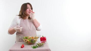 knubbig kvinna kock kastar en körsbär tomat sexig äter den ler gör ögon på en vit bakgrund Plats för reklam text renlighet städning förkläden handskar visar tumme upp klass framställning en sallad video