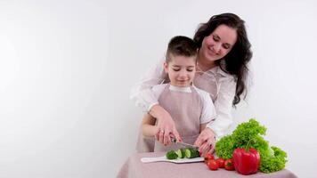 bonding concept. vrolijk moeder helpen haar zoon naar koken, onderwijs weinig jongen hoe naar bereiden gezond groente salade, Koken samen Bij huis. onderwijzen een jongen naar besnoeiing komkommer video