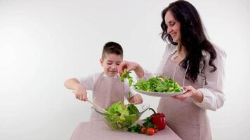 mom and son cooking fresh vegetable salad leaves smiling matching clothes apron white background studio space for text grocery store ad restaurant home food spending time with kids care love video
