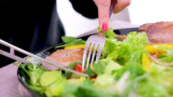 A girl eats vegetable salad with a fork from a white plate. Close up shot video