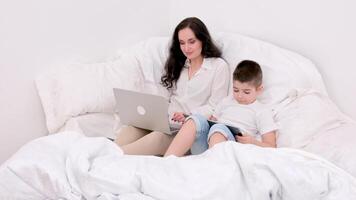 mom and son under blanket playing on tablet laugh smile games internet online learning educational activities spend time together in the family at home recover skip school at kindergarten day off video