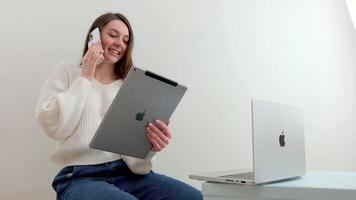 iPad MacBook lächelnd weiblich Schüler trägt kabellos zu Studie online mit ein Skype Lehrer, glücklich jung Frau lernt ein Sprache, Hör mal zu zu ein Vorlesung Uhr ein Webinar, schreiben Anmerkungen, aussehen beim ein Laptop video