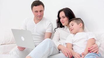 familj och son tittar på och spela läsplatta på säng familj Sammanträde på de soffa ser på bärbar dator, studio skott video