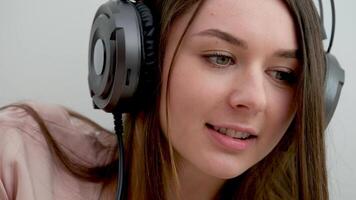 närbild ansikte av en flicka i hörlurar arbetssätt på Hem lyssnande till musik med hörlurar i henne fredlig Hem. närbild porträtt av ung kvinna lyssnande till musik med hörlurar.långsam rörelse . video
