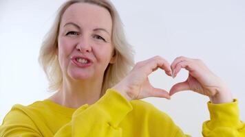 Smiling blond girl in yellow sweater showing heart with two hands, love sign. Isolated over white background. video