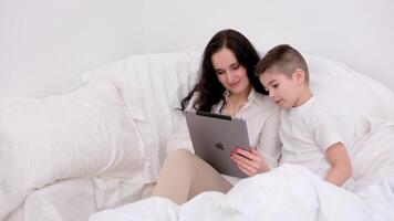 Junge, und seine Mutter ist Arbeiten auf ein Laptop Computer, das wenig Junge stellen das Tablette im seine Hand und gedreht zu seine beschäftigt Mutter aufmerksam, wollen seine Mutter zu Zahlen Beachtung zu ihn. video