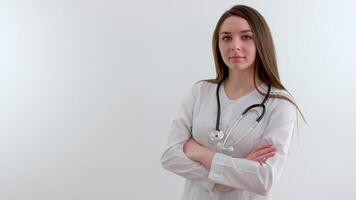 lindo fêmea médico dentro branco casaco olhando às Câmera e sorridente enquanto em pé com cruzado braços video