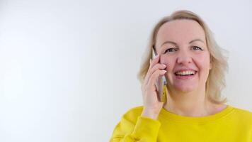 content femme en portant une téléphone intelligent et gagnant le prix. une femme dans une Jaune veste est parlant sur téléphone en riant en dehors bruyant lot de joyeux émotions incroyable blanc Contexte côté vue bien qualité video