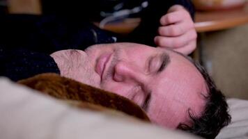 barbudo homem com dor de cabeça acordando acima e tocante face enquanto deitado em sofá perto balões e confete depois de festa às casa video