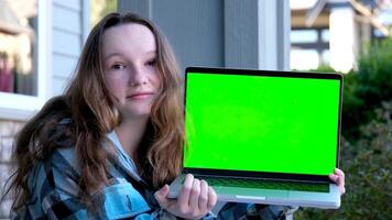 Portrait studio shot of young hipster female model in casual street wears sunglasses sit on floor holding pointing green blank empty screen laptop computer for advertising video