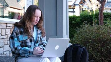 Girl university student wearing headphones using smartphone app sitting on stairs outdoors online learning, remote studying virtual class, watching webinar distance course or listening podcast. video
