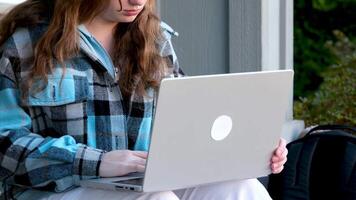 Bild von ein jung schön froh Frau lächelnd während Arbeiten mit ein Laptop draußen auf das Veranda schön jung Teen Mädchen video