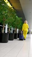 arriving or departing at airport woman with suitcase on wheels in hands hand luggage communication waiting night outside window walk down corridor middle-aged blonde real people Amsterdam airport video